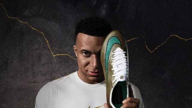 Kylian Mbappé segurando uma chuteira Nike Mercurial dourada e verde ao lado do rosto, fundo escuro com rachaduras douradas